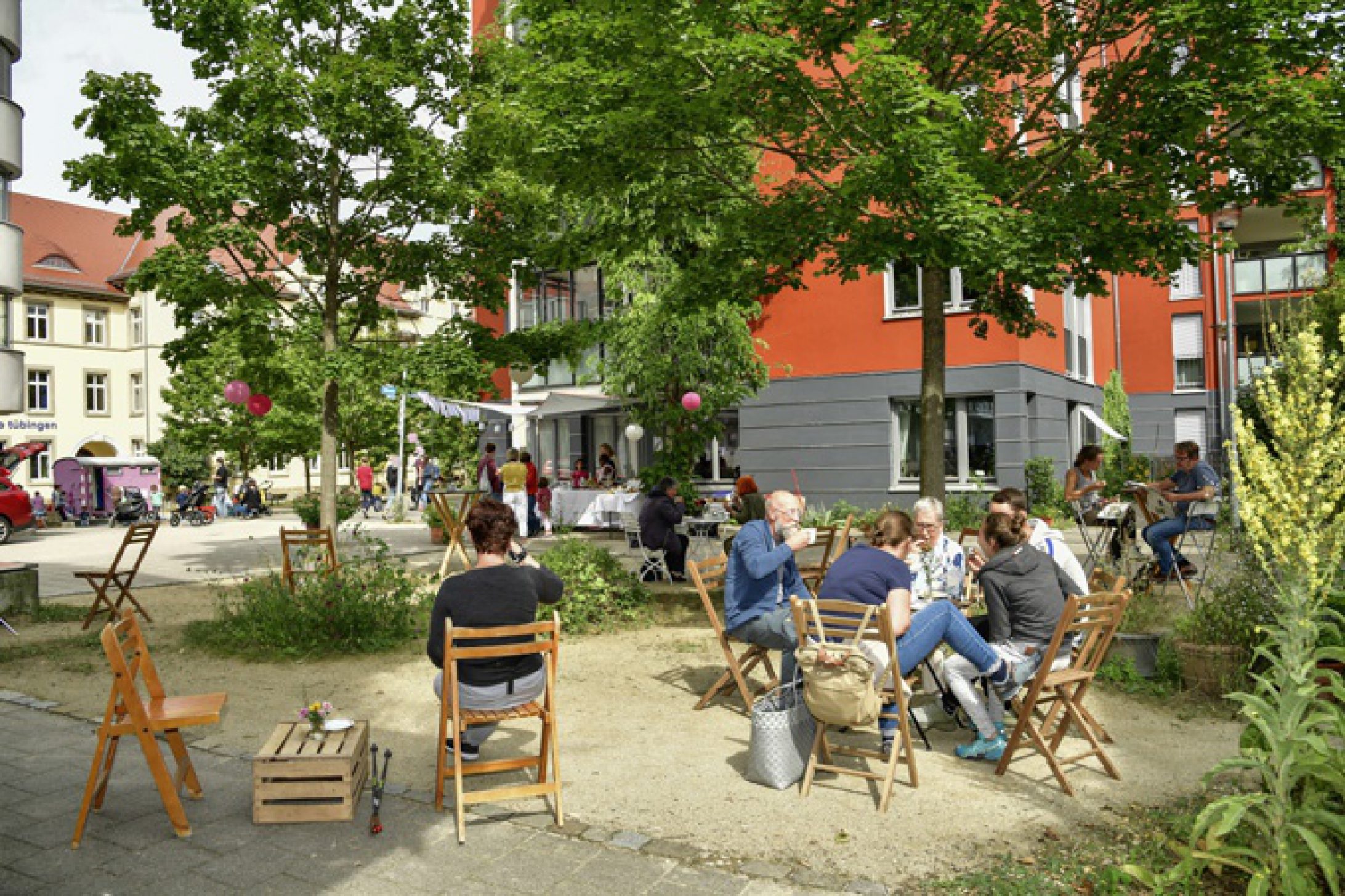 Bewohner des Stadtteils sitzen bei gutem Wetter gemeinsam im Hof unter Bäumen und führen Gespräche